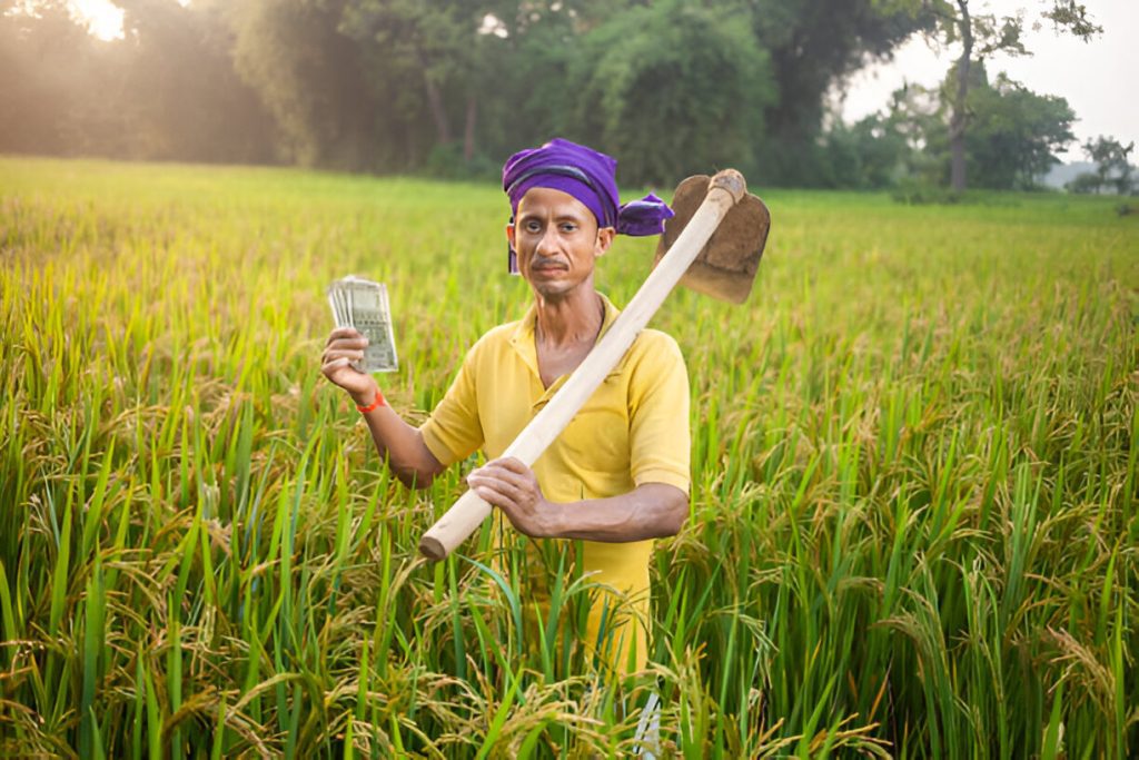 A man stands in a field, holding indian currency and a shovel, illustrating the concept of MGNREGA wage rates.