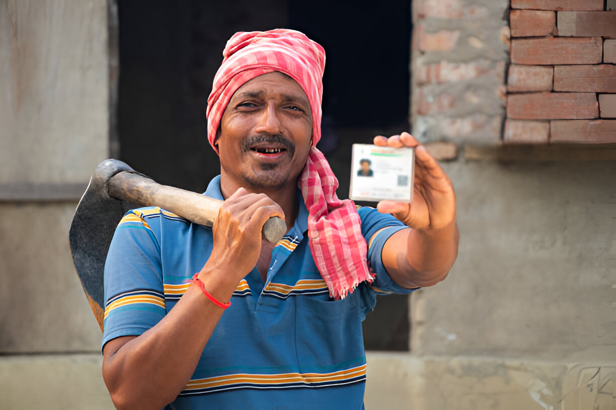 A man holds a small piece of paper displaying MGNREGA wage rates, emphasizing the importance of fair compensation.