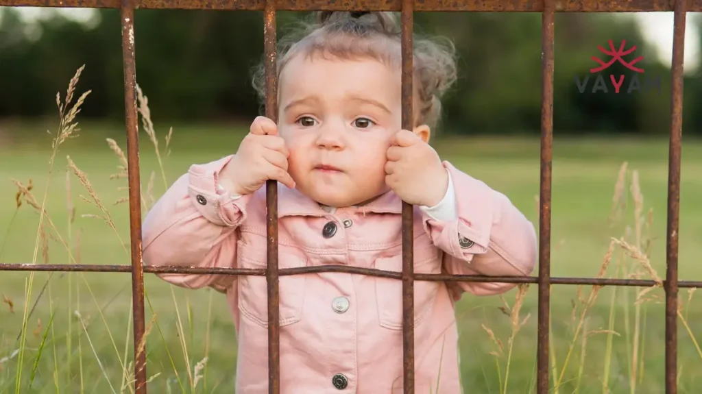 A baby girls are still at risk gazes through a fence, highlighting the ongoing risks faced by young girls everywhere.