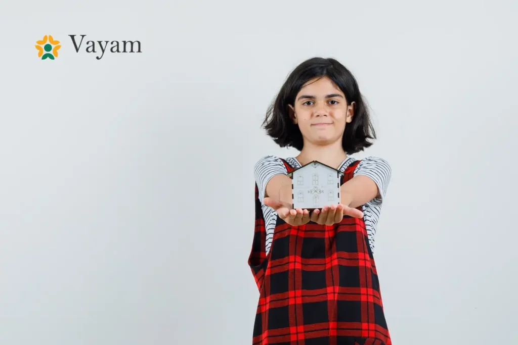 A young girl proudly holds a small house model, symbolizing hope and empowerment through NGO is changing girls lives.