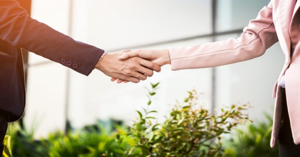 Two people shaking hands in front of a building, symbolizing CSR programs and maintaining long-term corporate partnerships.