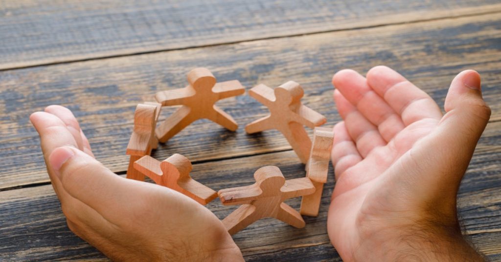 Hands grasp wooden people on a table, representing collaboration and the importance of CSR Funding.