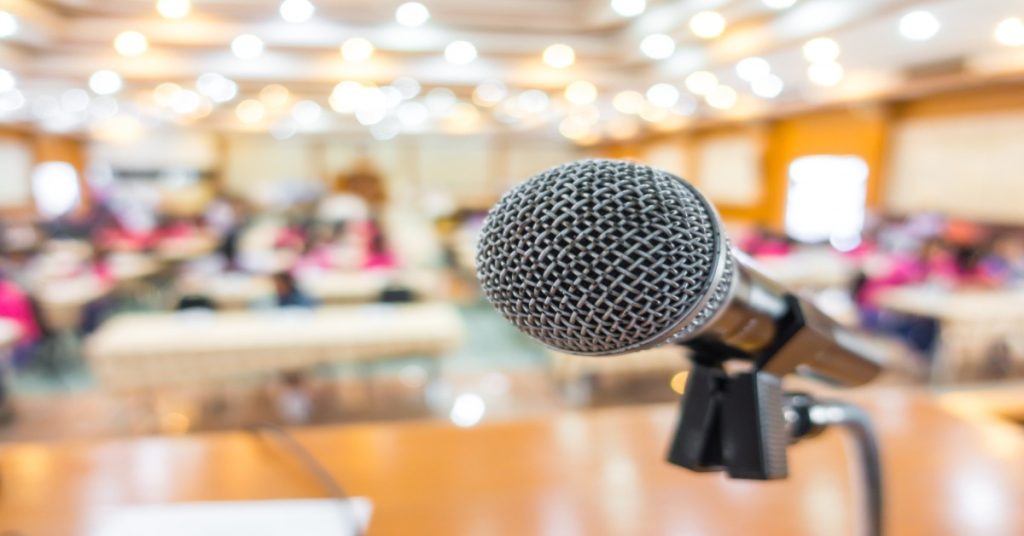 A room scene featuring a microphone and people, illustrating the importance of public speaking as a key skill.