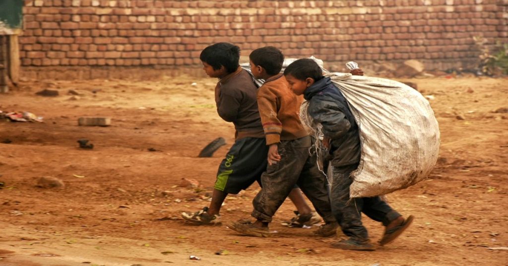 Three children carrying a large bag on their back, highlighting the issue of human trafficking and child labour.