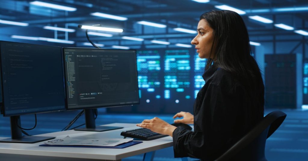 A woman at a desk with two monitors, focused on skill development in coding and programming bootcamps.