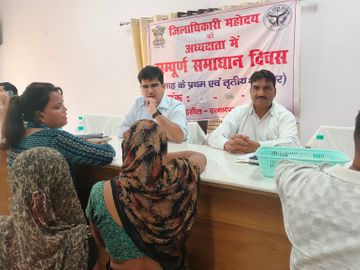 A group of people seated at a table in front of a panchayats banner, for grievance redressal.
