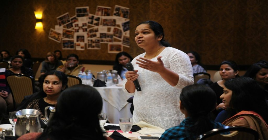 A woman speaks at a conference, inspiring a group of women in an empowerment program.