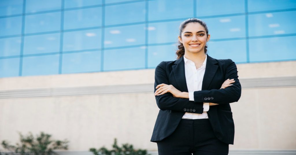 Young woman in corporate clothing standing in front of a building, representing future female leaders.