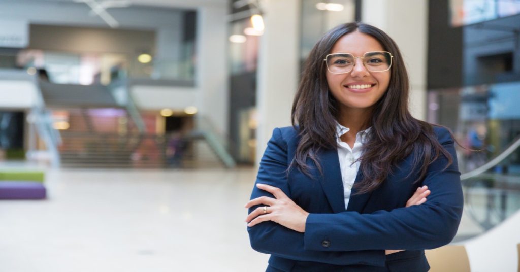 A woman wearing glasses and a business suit stands in a lobby, symbolizing the empowerment program's mission.