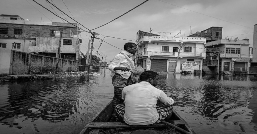 A boat with two men on a flooded street, emphasizing the difficulties faced in disaster relief operations.