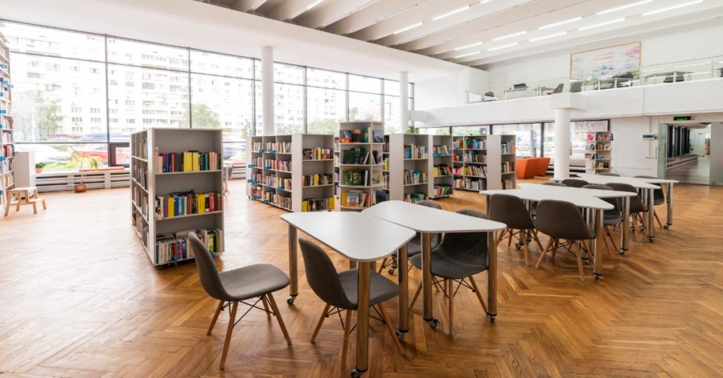 A library featuring tables and chairs by large windows, showcasing premium facilities that enhance the learning environment.