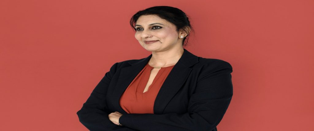 A professional woman over 40 in a red shirt and suit poses against a red background, representing career change opportunities.